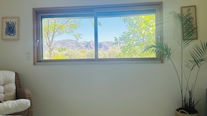 Ein Schlafzimmer mit großem Fenster, einem Korbstuhl, einem Bett und einer Topfpflanze.