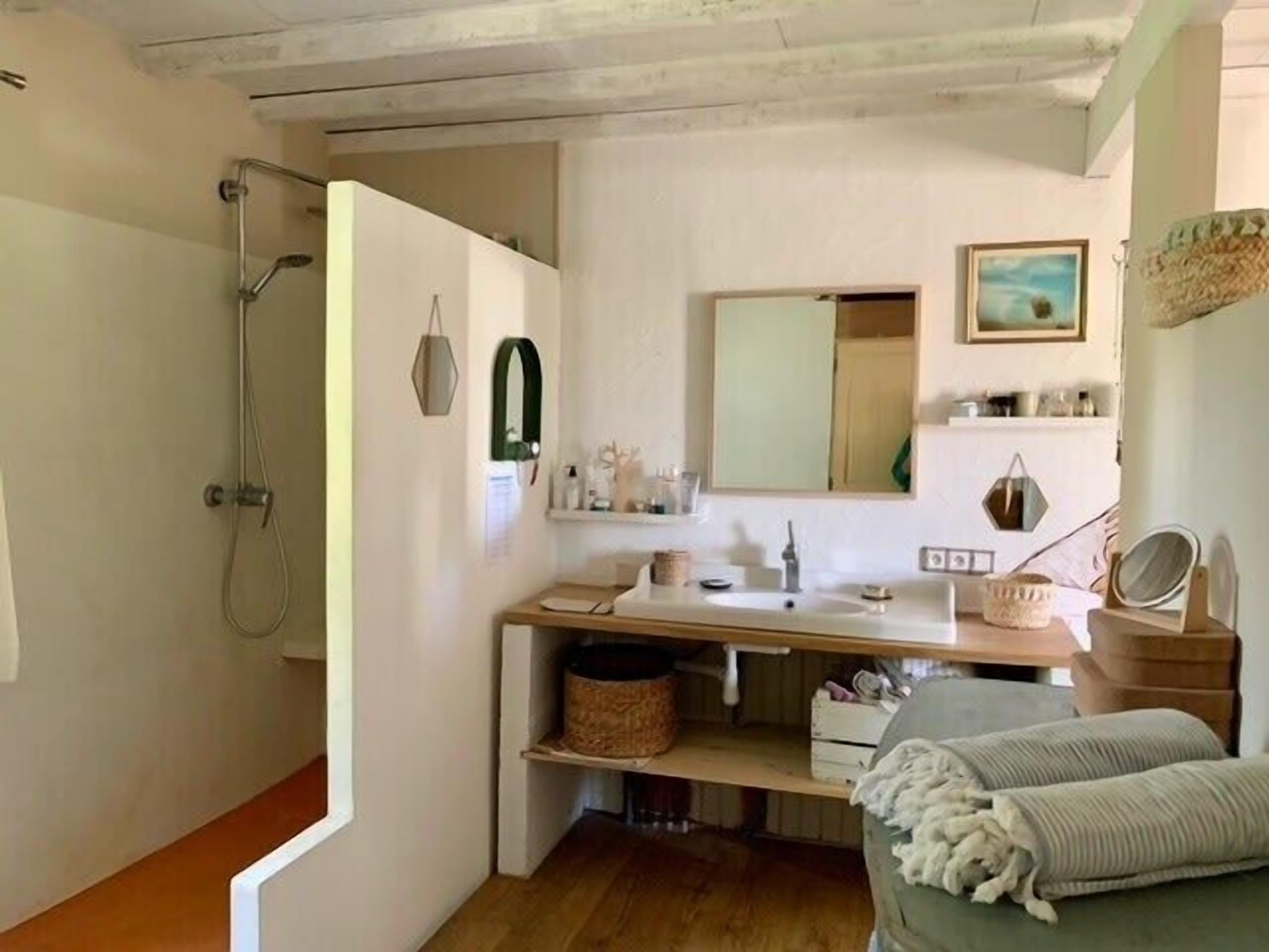 A bathroom with a shower, a sink, a mirror, and a shelf with toiletries.
