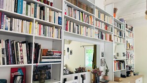 Ein Zimmer mit mehreren weißen Bücherregalen voller Bücher, einem Holztisch mit Lampe und einem Spiegel, der den Raum widerspiegelt.