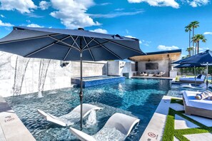 A swimming pool with lounge chairs and umbrellas, surrounded by a modern building with a poolside area. - NEW|Private Waterpark Estate | Lazy River & Grotto (Scottsdale)