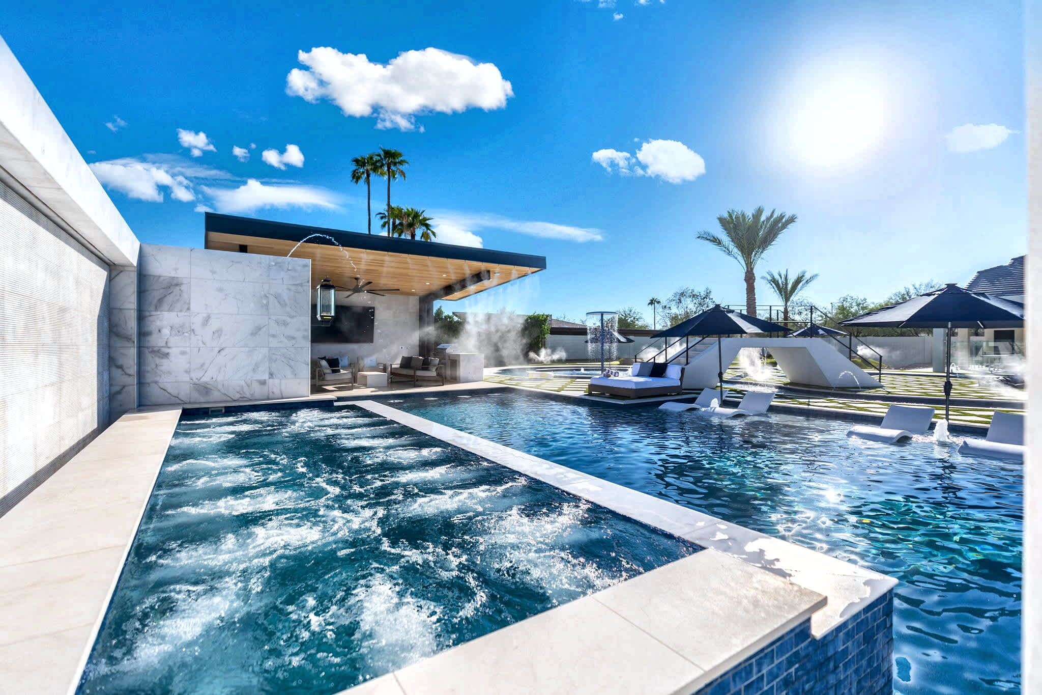 A modern outdoor pool area with a built-in hot tub, lounge chairs, and a covered seating area.