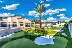 A golf course with a clubhouse, palm trees, and a clear blue sky. - NEW|Private Waterpark Estate | Lazy River & Grotto (Scottsdale)