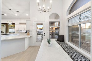 A modern kitchen with a central island, pendant lighting, and a view of an outdoor patio. - NEW|Private Waterpark Estate | Lazy River & Grotto (Scottsdale)