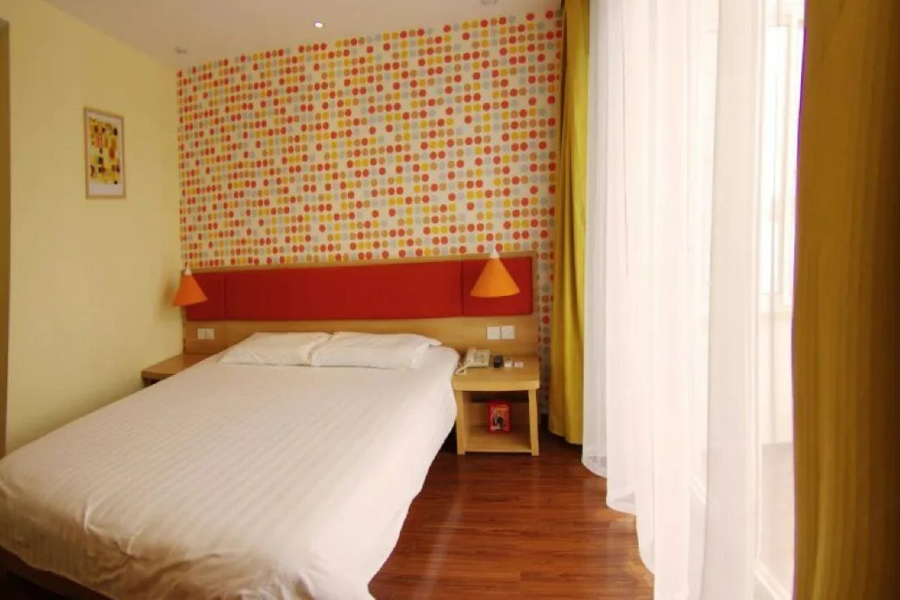 Une chambre d’hôtel avec un grand lit, une tête de lit rouge, deux lampes de chevet, une petite table de chevet et un mur à motifs.