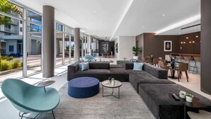 Een ruime lobby met een modern design, met een groot zithoek met banken en stoelen, een bijzettafeltje en uitzicht naar buiten.
