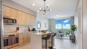 Een moderne keuken met een centraal eiland, roestvrijstalen apparatuur en een groot raam met uitzicht op een balkon.