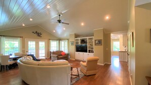 A spacious living room with a curved white sectional sofa, a ceiling fan, and a built-in entertainment unit. - Private home on the bank of the White River (Flippin)