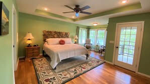 A bedroom with a bed, a ceiling fan, a nightstand, a lamp, a chair, a small table, and a door with a view of the outside. - Private home on the bank of the White River (Flippin)