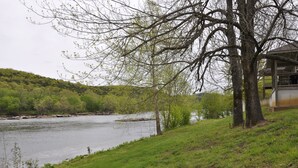 A riverside view with a grassy area, a tree, and a building with a balcony overlooking the water. - Private home on the bank of the White River (Flippin)