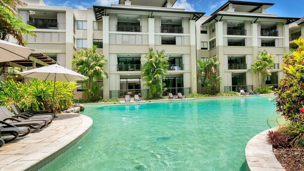 Un hotel moderno con piscina cristalina, tumbonas y palmeras.