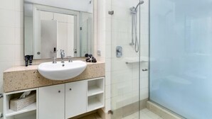 A modern bathroom with a white sink, a large mirror, and a glass-enclosed shower area. - Ground floor Spa Suite in the popular Beach Club Resort in Palm Cove (Palm Cove)