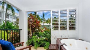 A balcony with a wooden chair and a bench, a white bathtub, and a door with white shutters. - Ground floor Spa Suite in the popular Beach Club Resort in Palm Cove (Palm Cove)