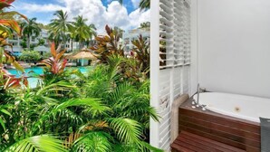 A balcony with a view of a pool and tropical plants, a white wall, and a bathtub. - Ground floor Spa Suite in the popular Beach Club Resort in Palm Cove (Palm Cove)