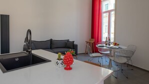 Uma cozinha moderna com pia, área de jantar com mesa e cadeiras, sofá e janela com cortinas vermelhas.
