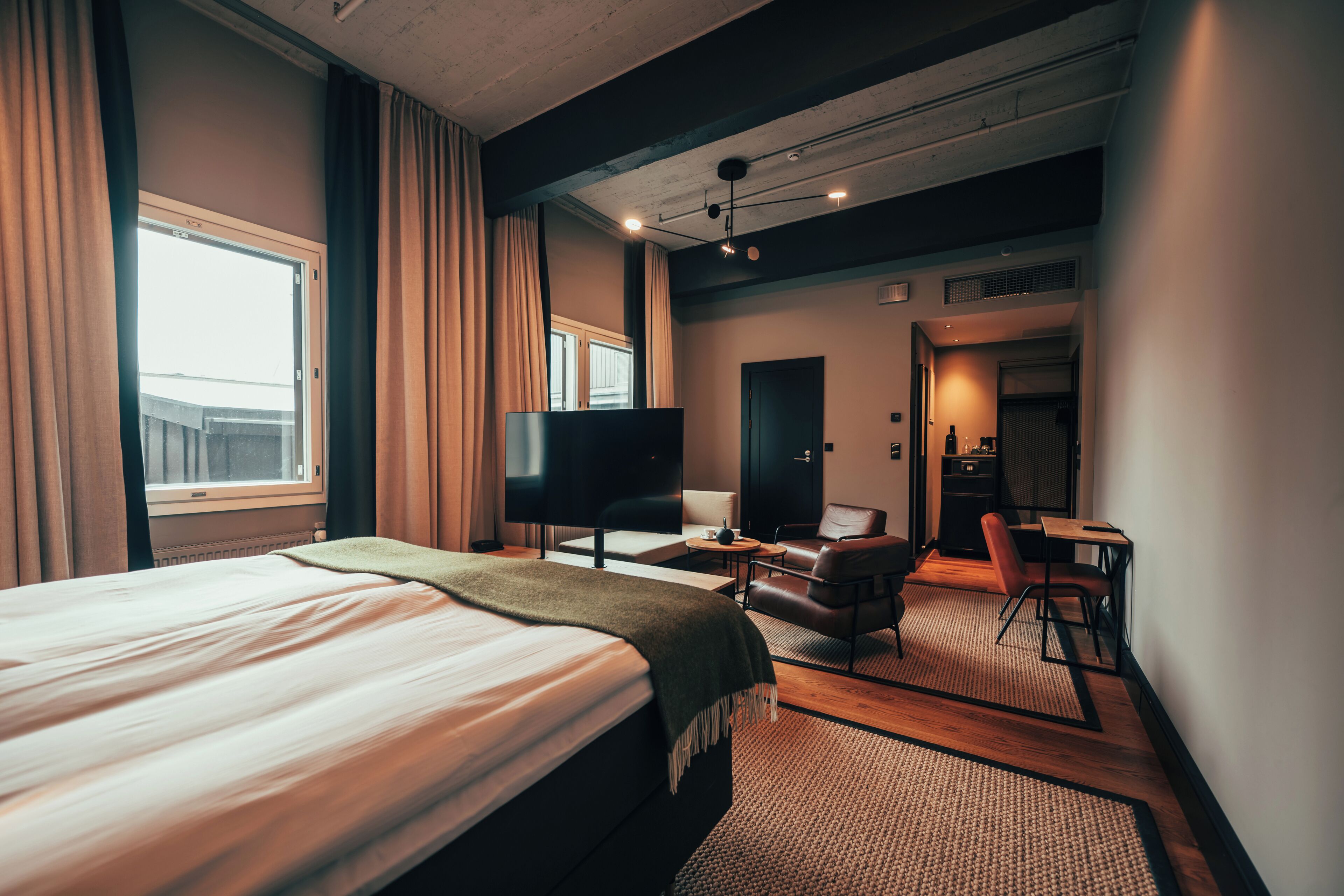 Habitación de hotel con cama, televisión, escritorio con silla y zona de estar separada con sillón y mesa.