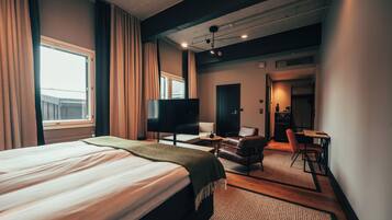 Habitación de hotel con cama, televisión, escritorio con silla y zona de estar separada con sillón y mesa.