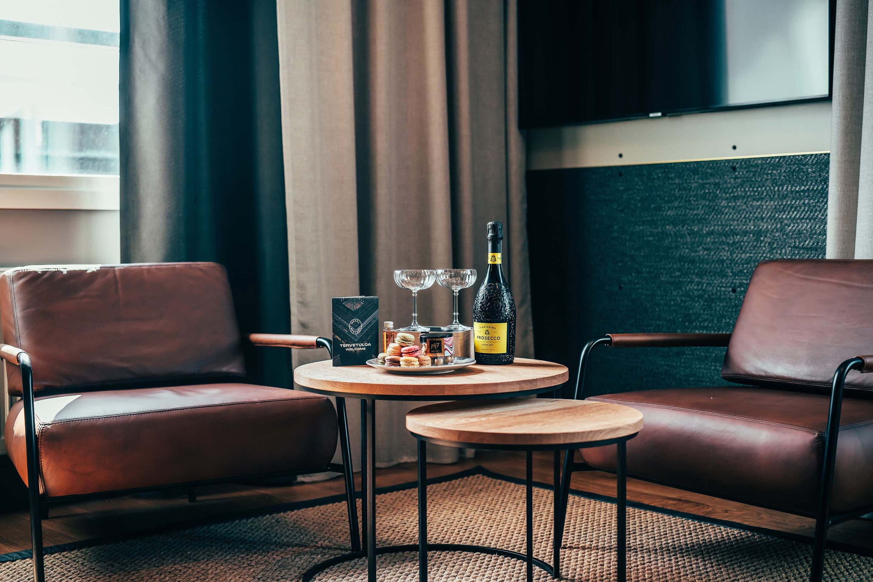 Una habitación moderna con dos sillones de cuero, una mesita de madera con una botella de vino, copas y una bandeja de aperitivos.