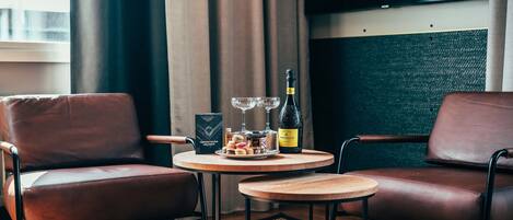 Una habitación moderna con dos sillones de cuero, una mesita de madera con una botella de vino, copas y una bandeja de aperitivos.