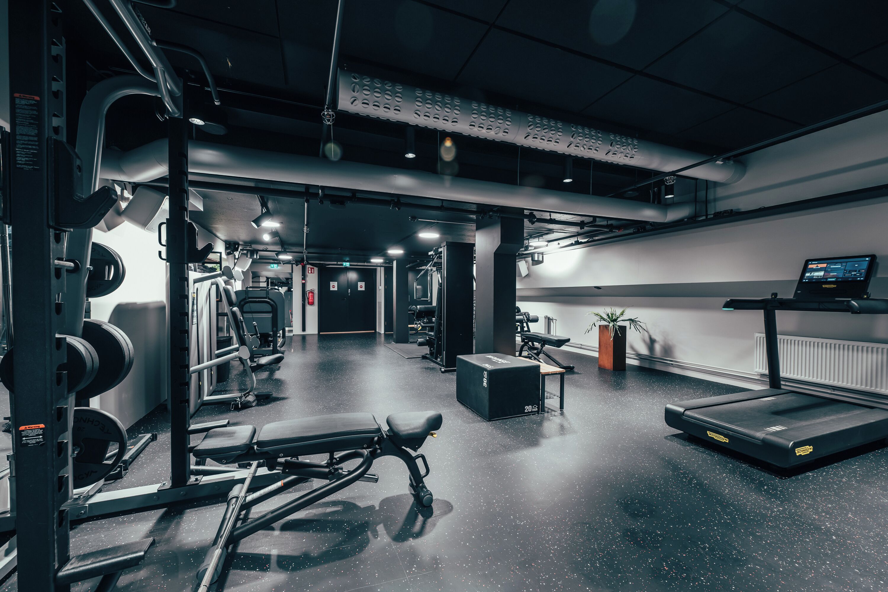 Een fitnessruimte met gewichthefapparatuur, loopbanden en banken.