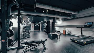 Een fitnessruimte met gewichthefapparatuur, loopbanden en banken.