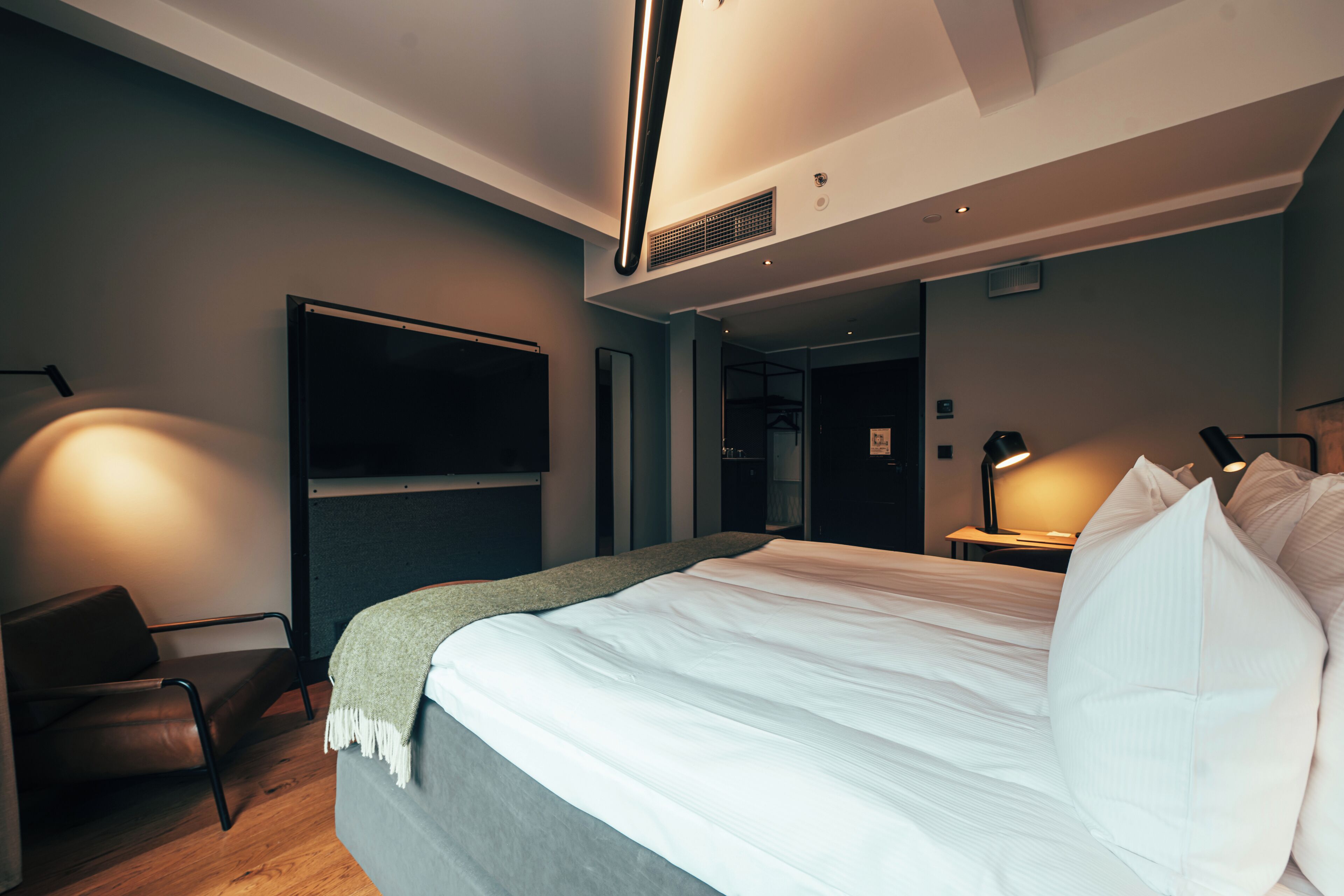 Una habitación de hotel moderna con una cama grande, un televisor de pantalla plana, un escritorio con lámpara y una silla.