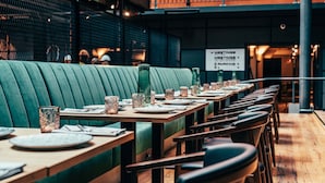 A restaurant with green upholstered booths, wooden tables, and metal chairs. - Clarion Hotel Mestari (Helsinki)