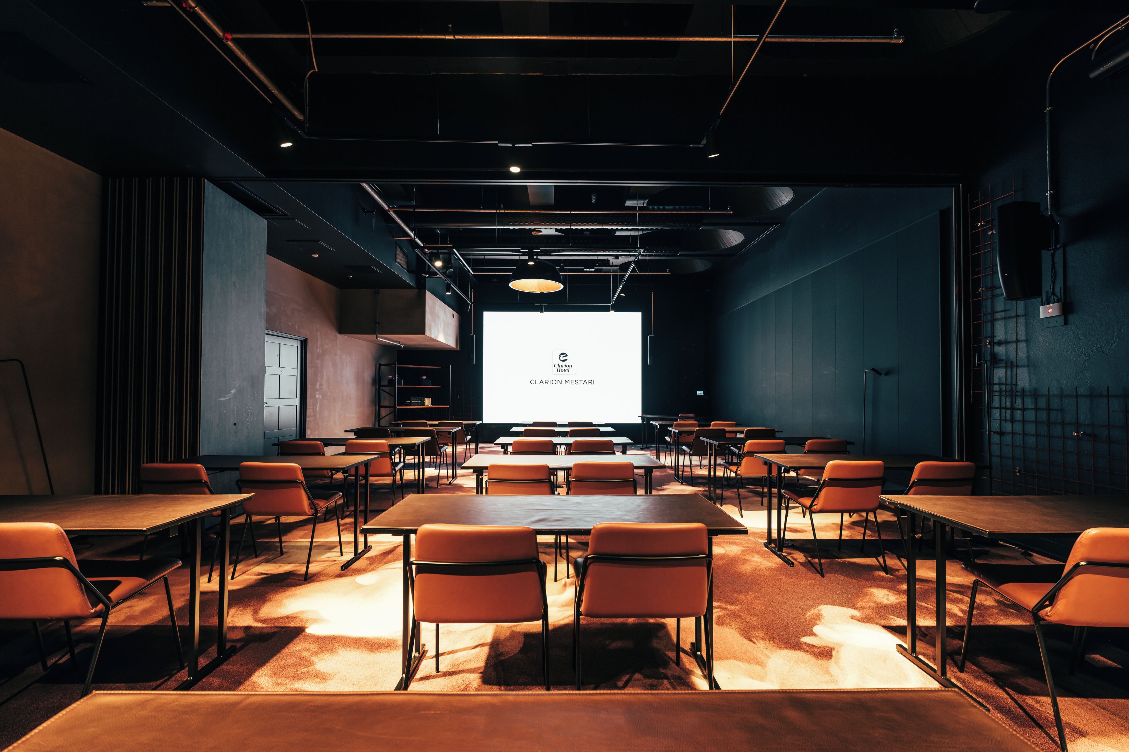 Une salle de conférence équipée de tables et de chaises, d’un grand écran et d’un projecteur.