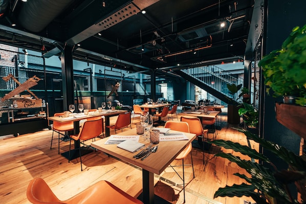 A modern restaurant with wooden tables and orange chairs, featuring a staircase and large windows. - Clarion Hotel Mestari (Helsinki)