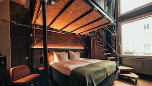 A modern bedroom with a loft bed, a staircase, and a view of the city. - Clarion Hotel Mestari (Helsinki)