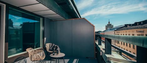 A balcony with wicker chairs and a small table, overlooking a cityscape.