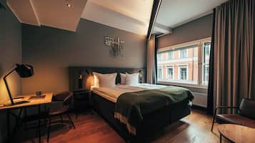 A modern hotel room with a bed, desk, chair, and a view of the city.