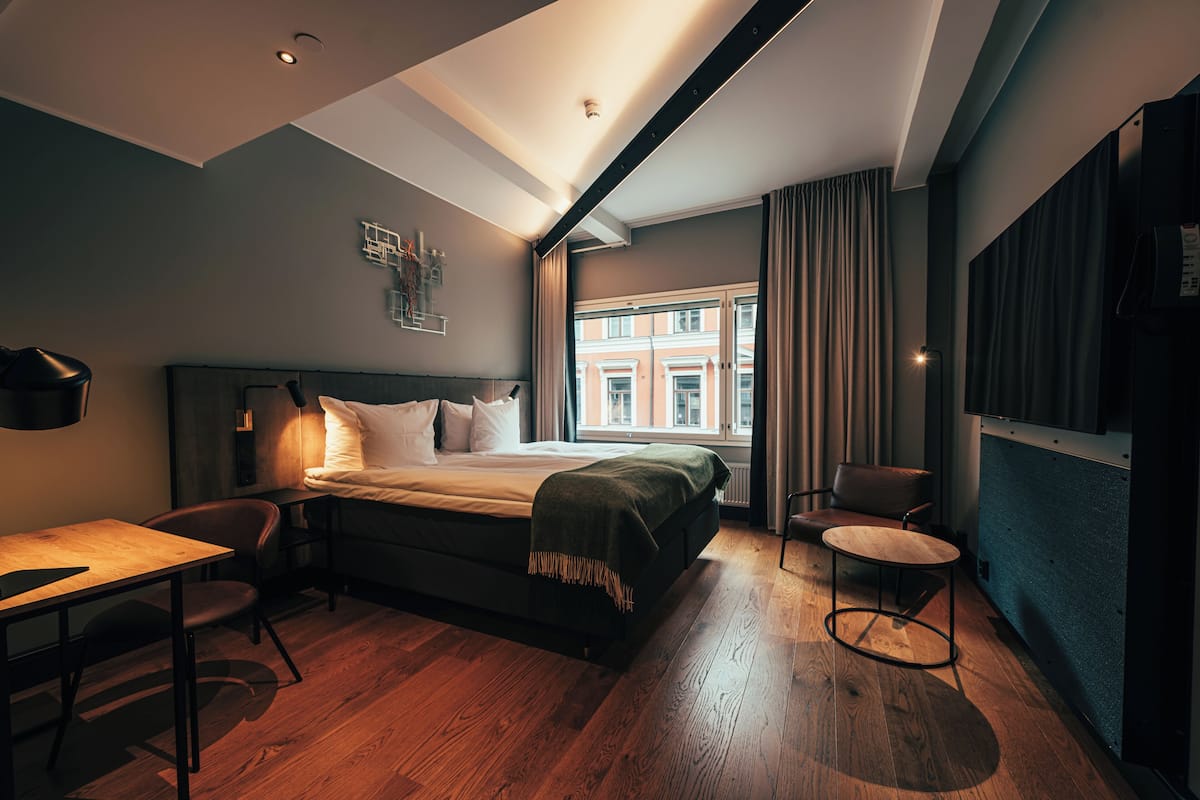Una habitación de hotel moderna con una cama grande, un escritorio, una silla y vistas a un edificio a través del ventanal.