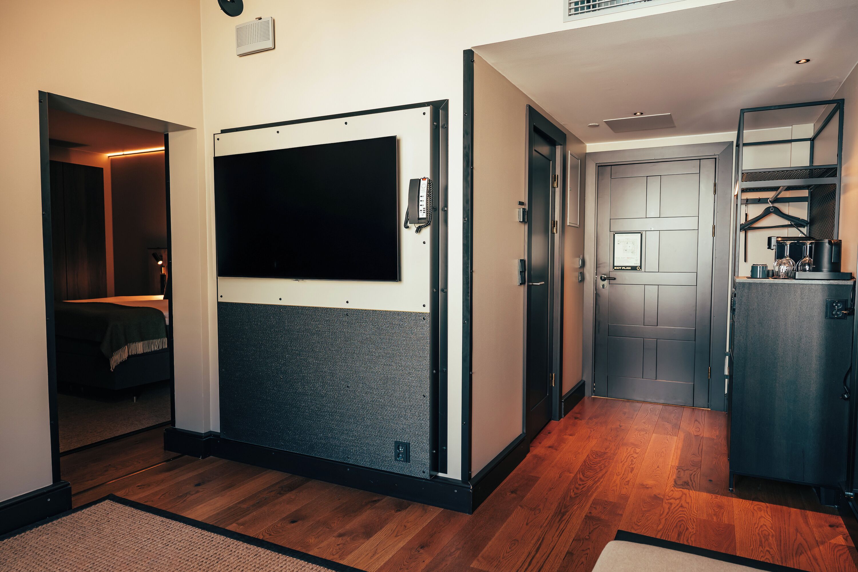 A hotel room with a large wardrobe, a bed, a desk, and a small kitchenette.