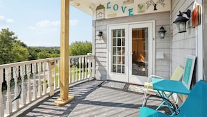 Une terrasse en bois avec une balustrade blanche, un porche couvert et une porte donnant sur une pièce.