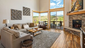 A spacious living room with a large sofa, a fireplace, and a view of the outdoors. - Mountain Willow At Grand Park 4 Bedroom Home by RedAwning (Fraser)