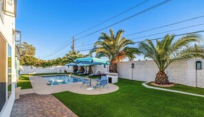 A backyard with a swimming pool, palm trees, and a patio area with chairs and umbrellas. - Private 5BR Resort | Pool, Hot Tub, En-suites (Scottsdale)