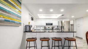 A modern kitchen with white cabinets, stainless steel appliances, and a bar area with stools. - Private 5BR Resort | Pool, Hot Tub, En-suites (Scottsdale)