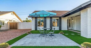 A patio with a table and chairs, a blue umbrella, and a small cactus garden.