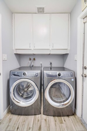 A laundry room with two front-loading washing machines, a white cabinet above, and a wooden floor. - Private 5BR Resort | Pool, Hot Tub, En-suites (Scottsdale)