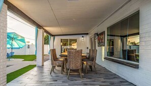An outdoor patio with a dining table and chairs, a blue umbrella, and a view of a garden. - Private 5BR Resort | Pool, Hot Tub, En-suites (Scottsdale)