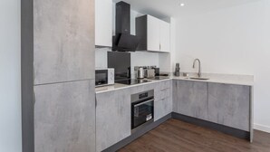 Eine moderne Küche mit grauen Schränken, einer Edelstahl-Dunstabzugshaube, einer Mikrowelle, einem Wasserkocher und einem Waschbecken.