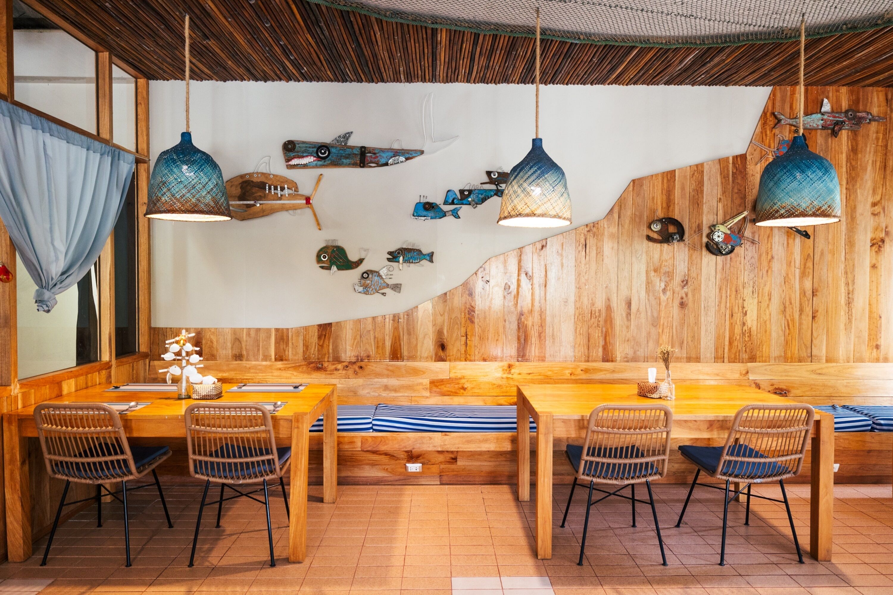 A restaurant with wooden walls, hanging pendant lights, and a long communal table with striped cushions.