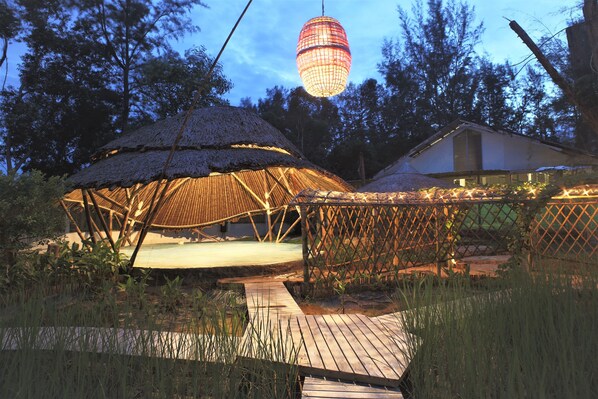 A thatched-roof structure with a wooden deck leading to it, surrounded by greenery. - Dugong Village-Green Hotel (Sikao)