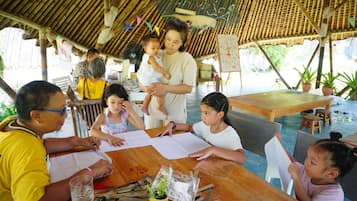 A group of people engaged in a craft activity under a thatched roof structure with tables and chairs.