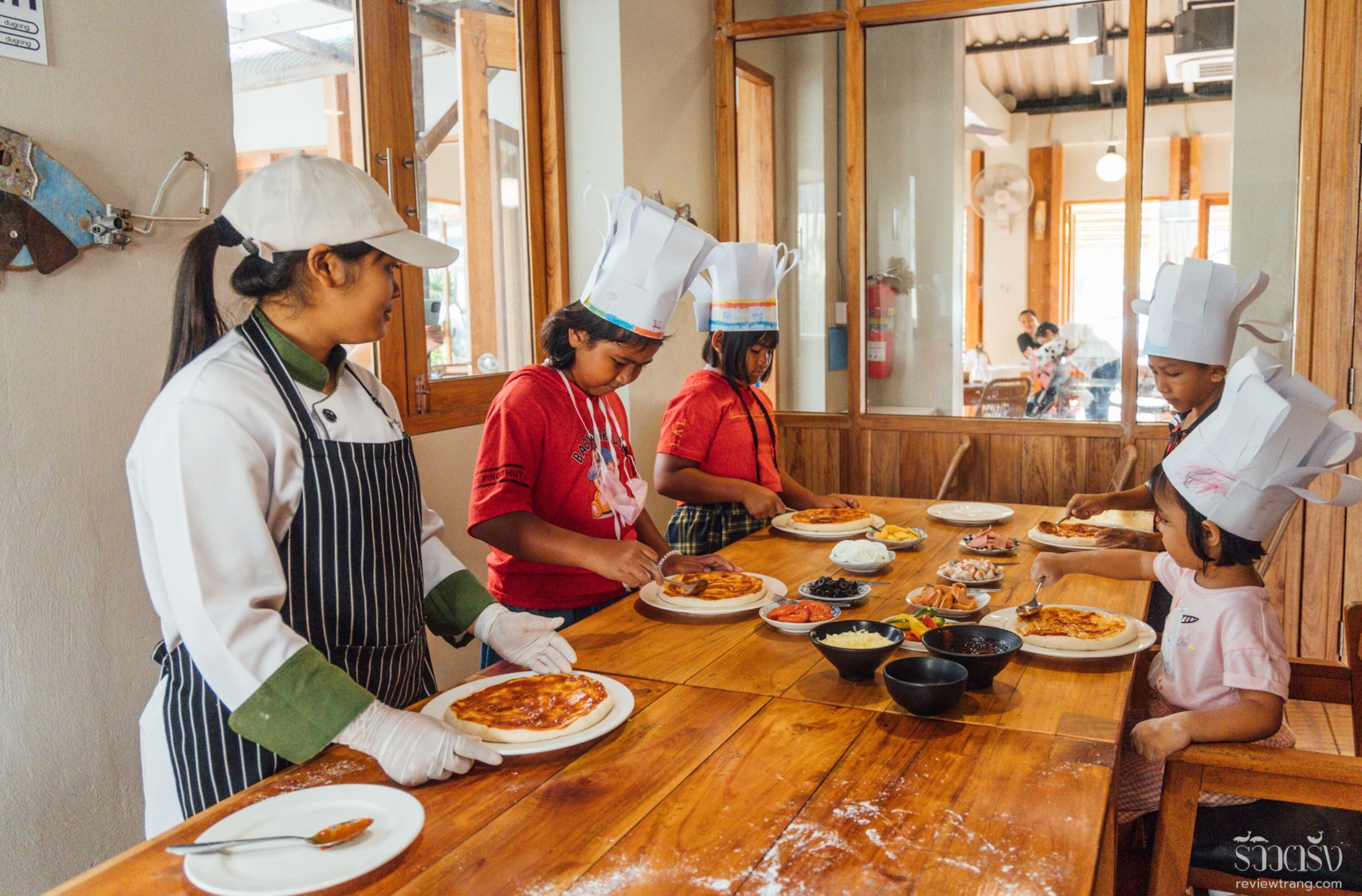 Un grupo de personas con gorros y delantales de chef alrededor de una mesa de madera llena de comida.
