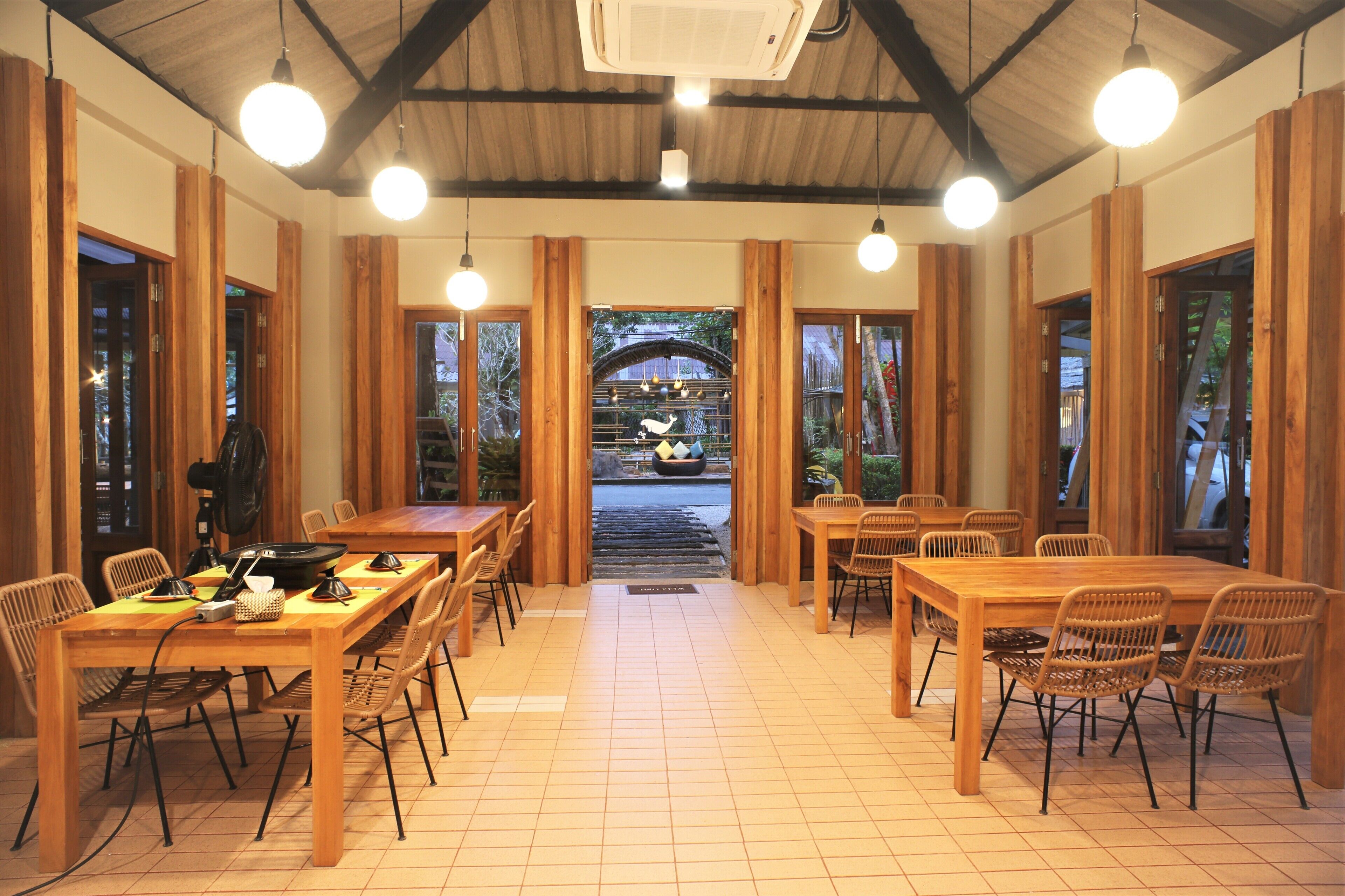 Un espace repas avec des tables et des chaises en bois, un passage central et de grandes fenêtres.