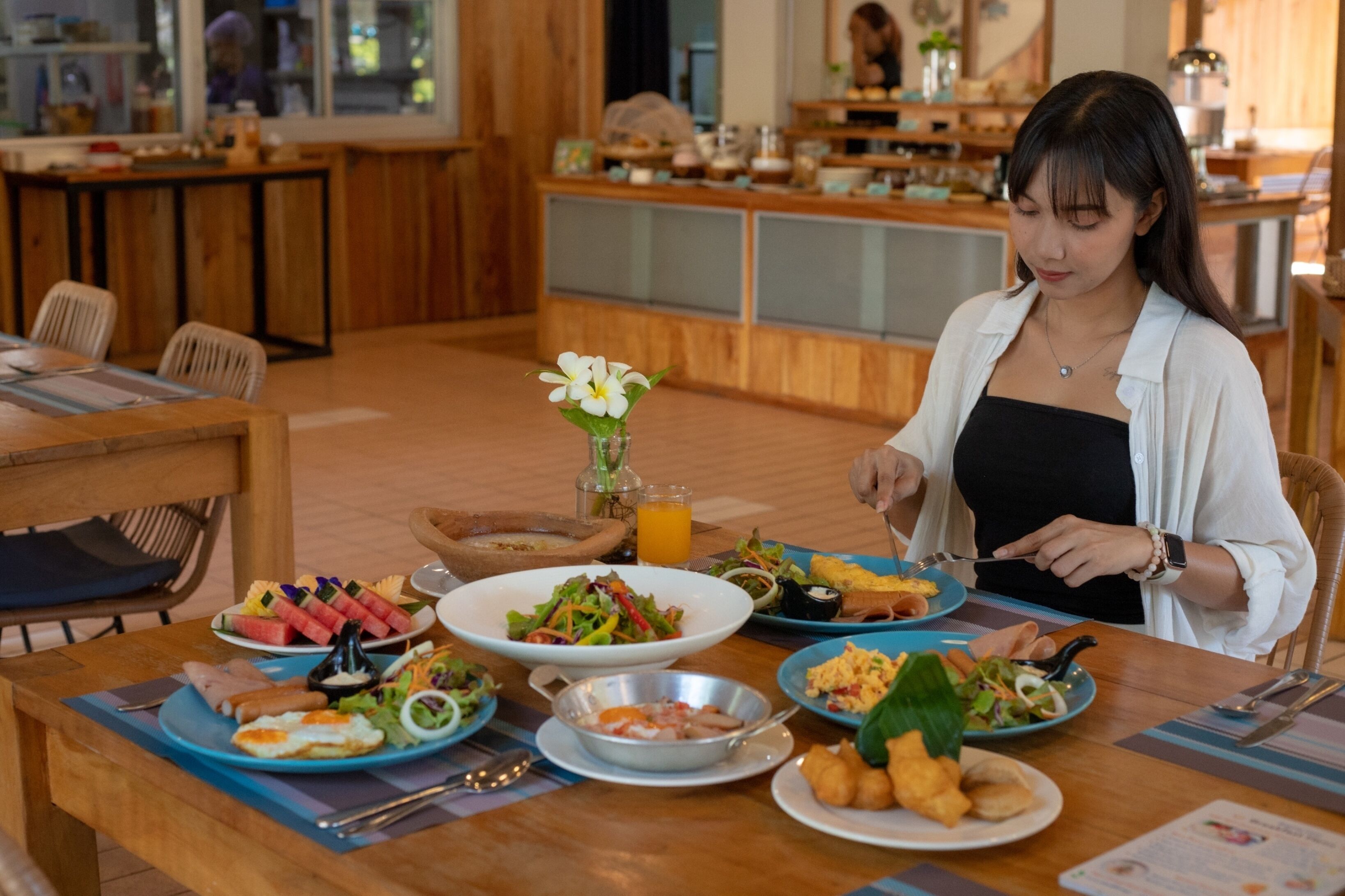 A breakfast buffet with various dishes and a woman eating.