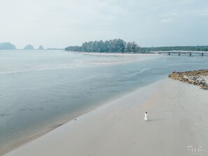 A beach with a person in a white dress walking along the shore. - Dugong Village-Green Hotel (Sikao)