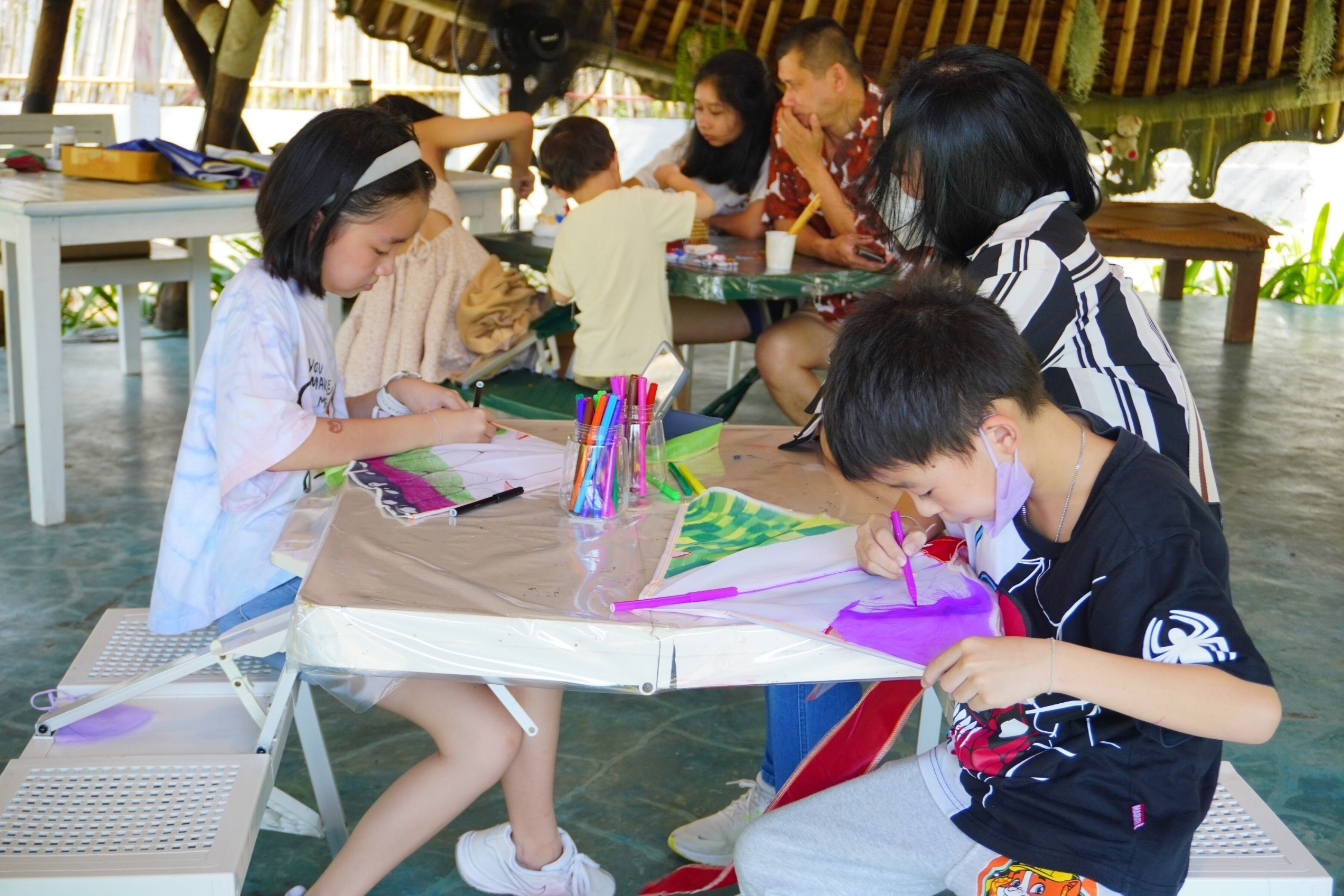 Un grupo de personas sentadas en mesas con materiales de arte, dedicadas a dibujar.