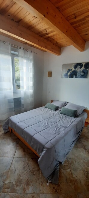 Un dormitorio con cama, cortinas, un cuadro y techo de madera.